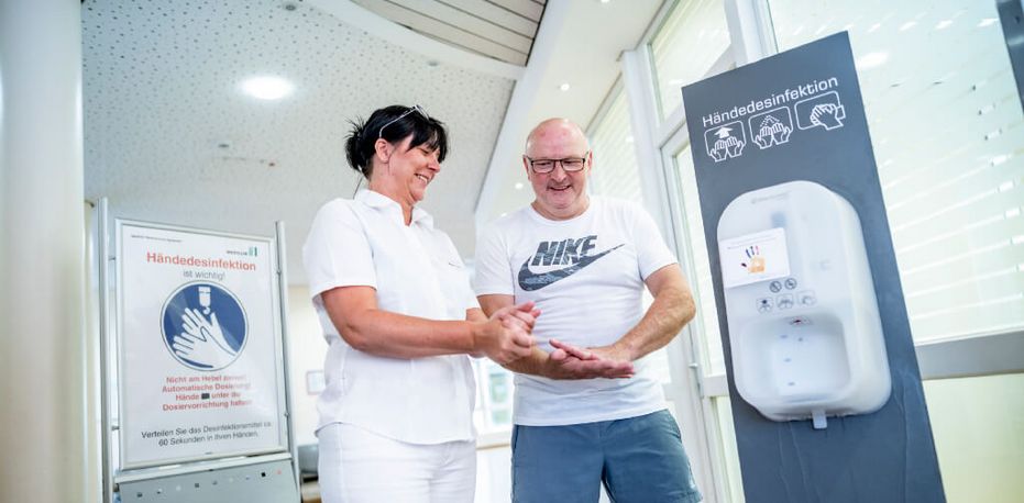 Pflegekraft zeigt Patient, wie er sich richtig die Hände desinfiziert