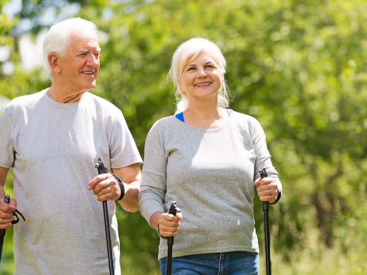 Fröhliches älteres Paar wandert mit Nordic Walking-Stöcken