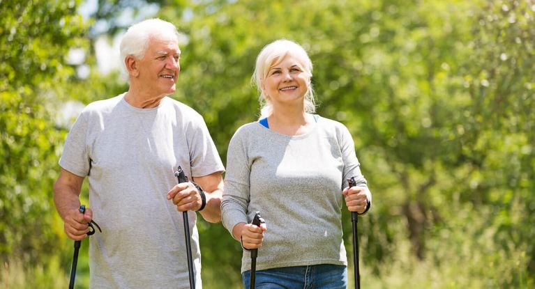 Fröhliches älteres Paar wandert mit Nordic Walking-Stöcken
