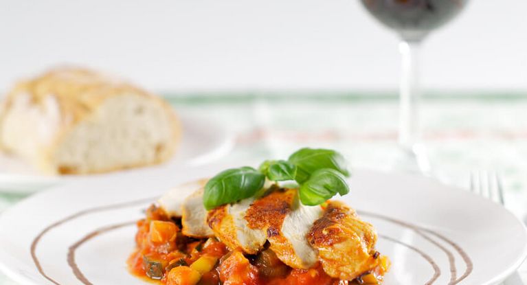 Eine Portion Hähnchenfilet mit roter Sauce und ein gefülltes Rotweinglas warten auf den Gast