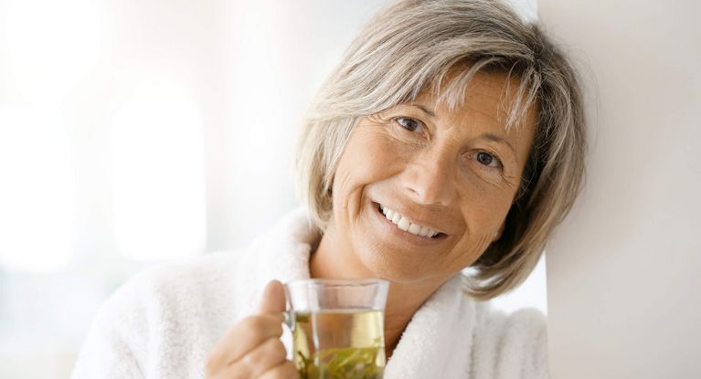 Ältere Frau im Bademantel hält eine gläserne Tasse mit Tee in den Händen