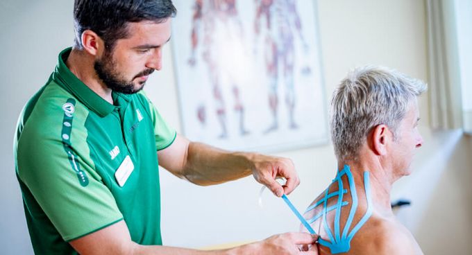 Therapeut klebt Kinesiotape auf den Rücken einer Patientin
