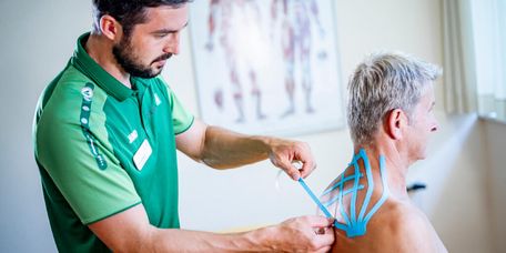 Therapeut klebt Kinesiotape auf den Rücken einer Patientin