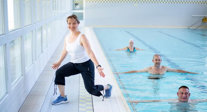 Therapeutin motiviert Patienten bei der Wassergymnastik in der Schwimmhalle