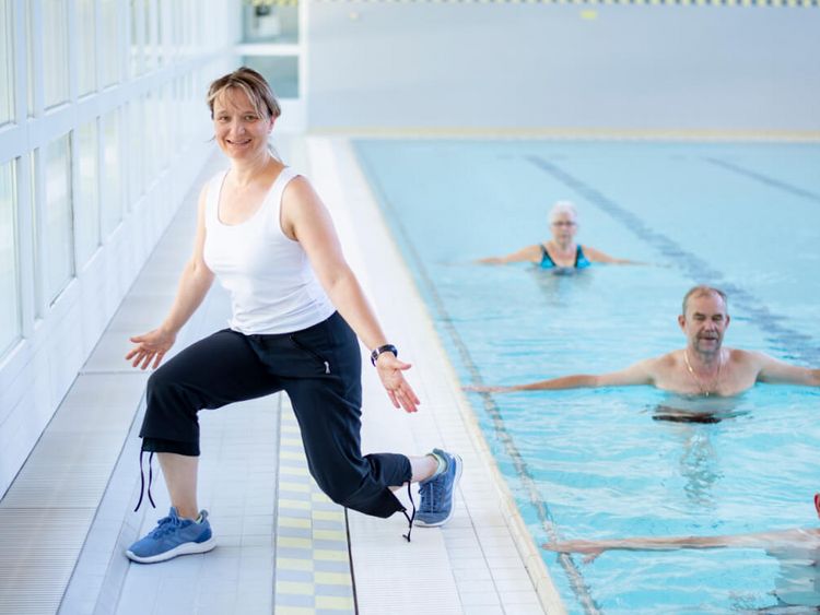 Therapeutin motiviert Patienten bei der Wassergymnastik in der Schwimmhalle