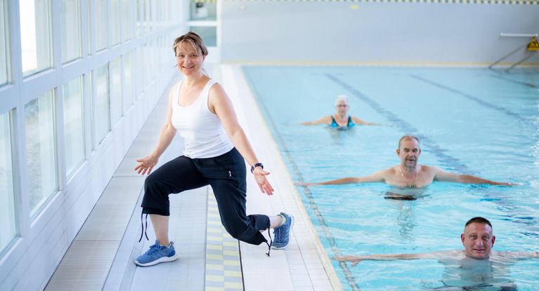 Therapeutin motiviert Patienten bei der Wassergymnastik in der Schwimmhalle