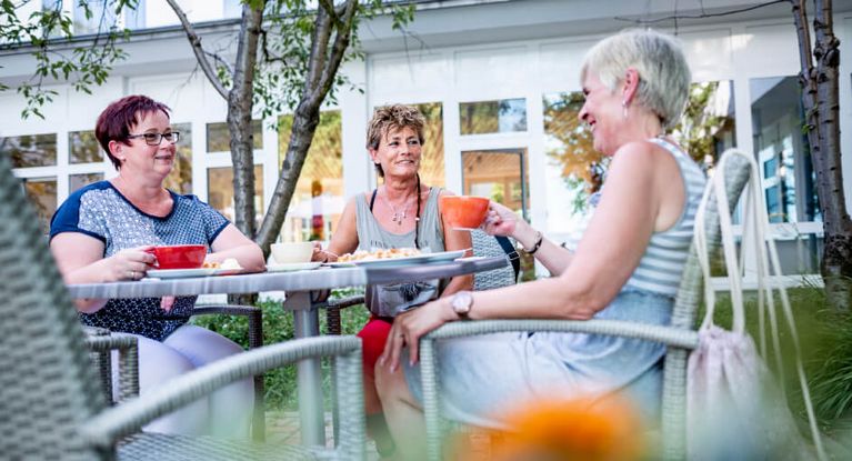 Patienten sitzen draußen am Tisch und trinken Kaffee