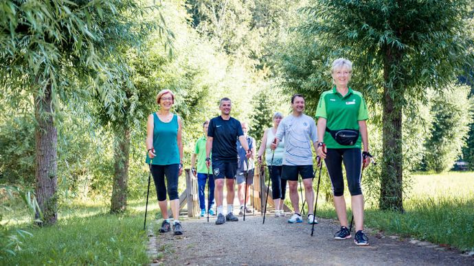Patientengruppe wandert beim Nordic Walking durch einen Park
