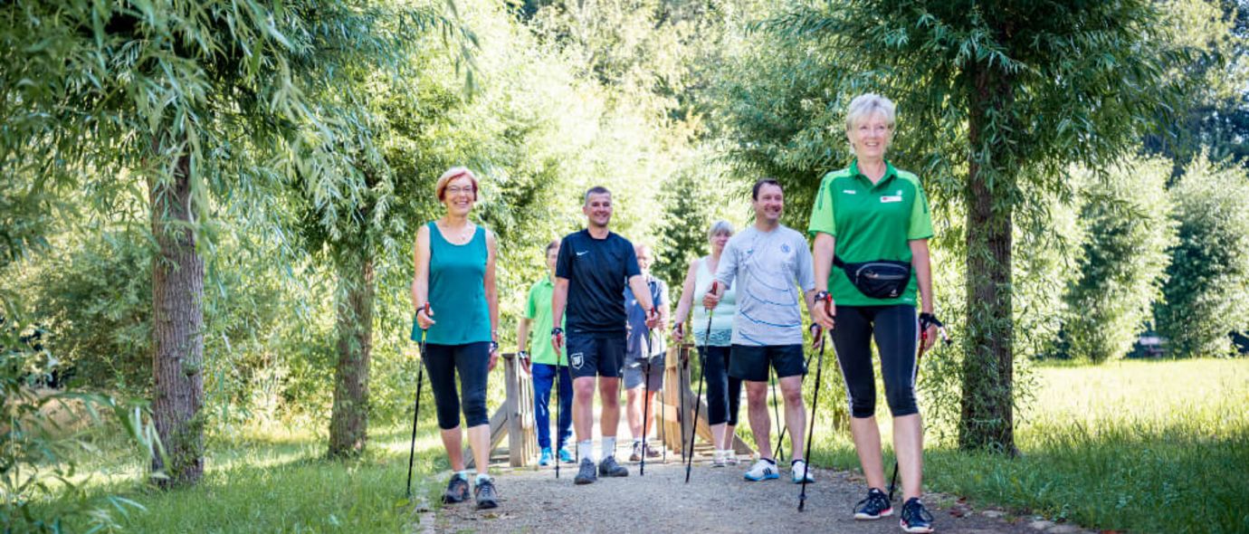 Patientengruppe wandert beim Nordic Walking durch einen Park